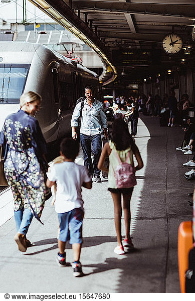 Family walking by train on railroad station platform