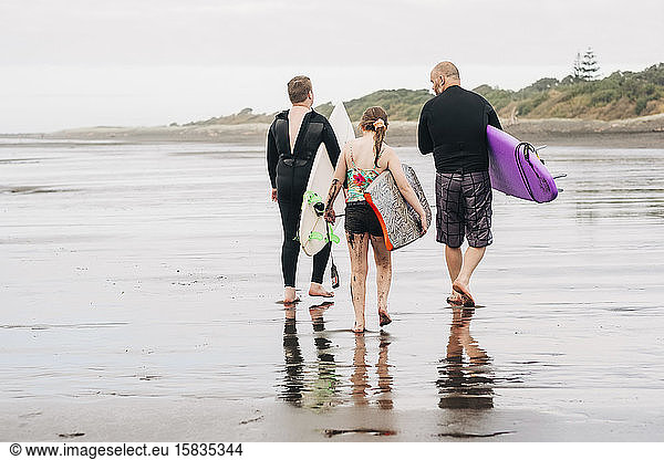 Family walking down the beach with boogie and surf boards