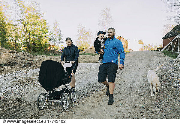 Family walking with dog and baby stroller on dirt road