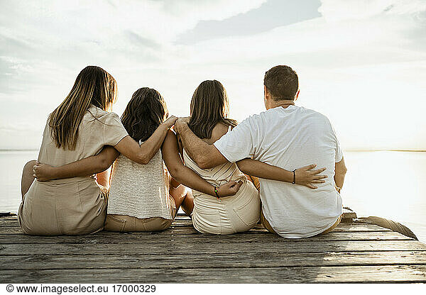 Family with arms around sitting on jetty at lake