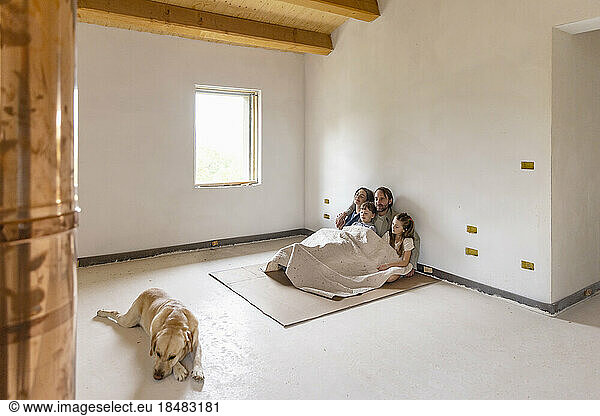 Family with blanket sitting together on cardboard at home