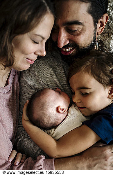 Family with closed eeditorial cuddled together embracing newborn