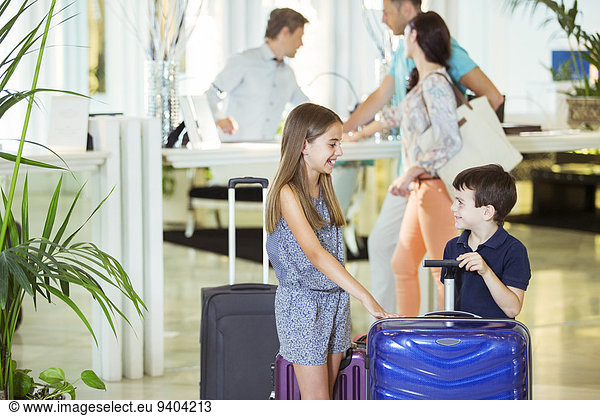 Family with daughter and son standing with suitcases in hotel lobby