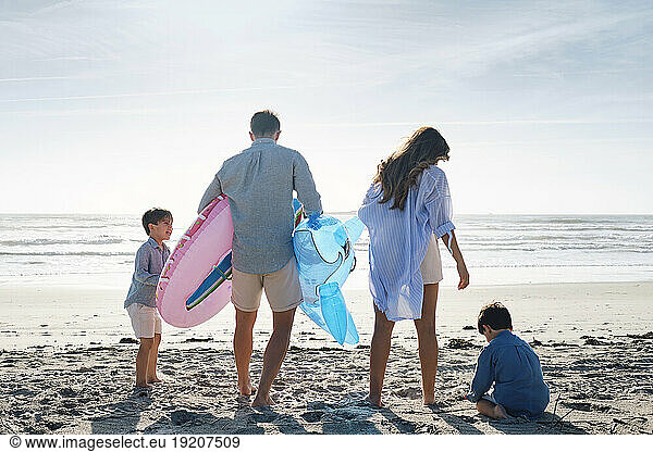 Family with inflatable swim ring and toy shark at beach on sunny day