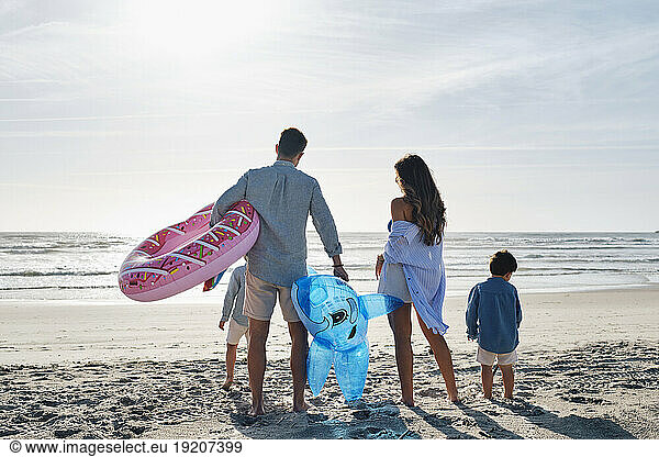 Family with inflatable swim ring and toy shark standing together at beach