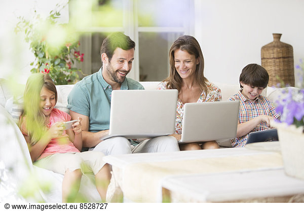 Family with laptops  digital tablet and cell phone on patio sofa