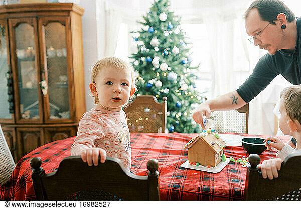 Family with little children decorating a gingerbread house in December