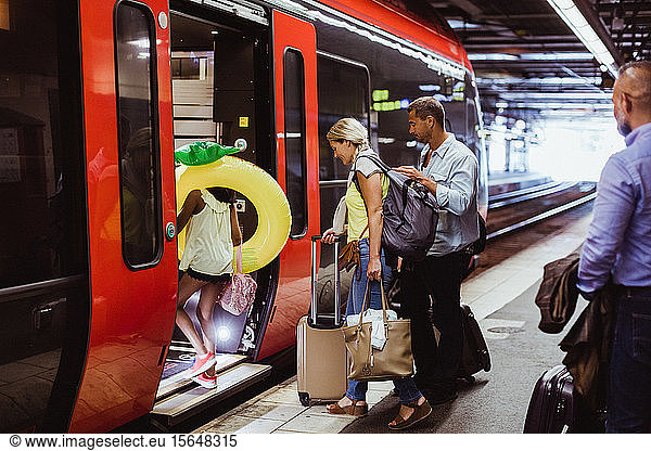 Family with luggage boarding train together at railroad station platform