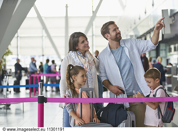 Family with suitcases pointing in airport concourse