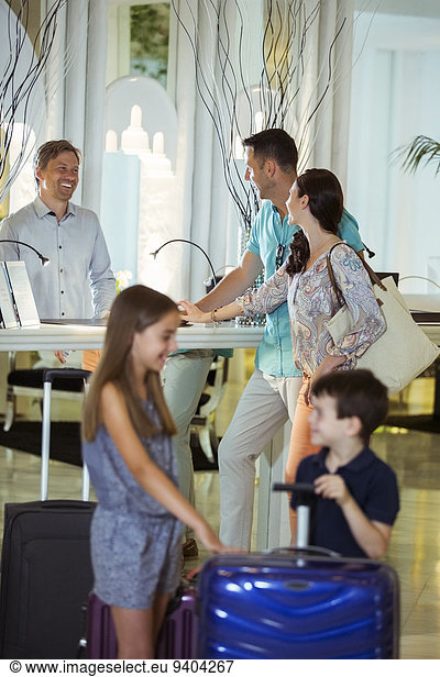 Family with suitcases talking with receptionist in hotel lobby