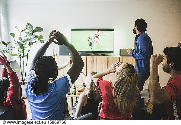 Fans cheering while watching soccer match on TV at home