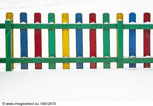 Farbenfroher Zaun eines Spielplatzes an einem verschneiten Tag.