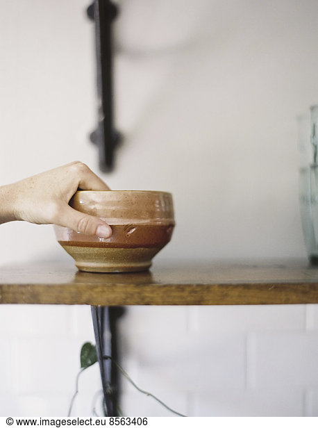 Farm to Table. A person reaching up for a pottery bowl in a domestic kitchen.