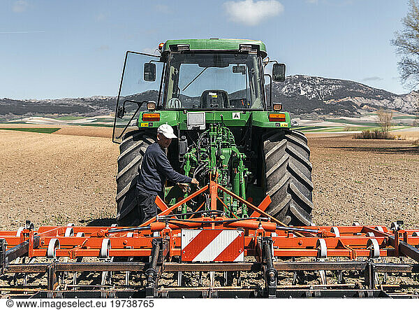Farmer adjusting plow of tractor standing in field