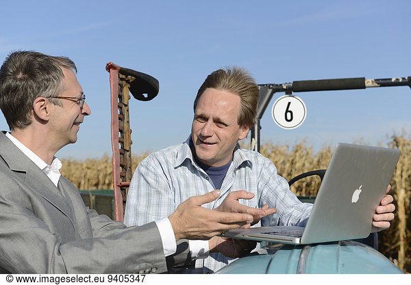 Farmer and businessman talking and checking information in laptop on cornfield