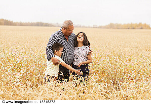 Farmer embracing grandchildren standing amidst crops in wheat farm