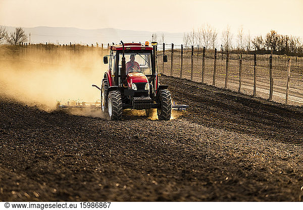 Farmer in tractor plowing agricultural land against sky