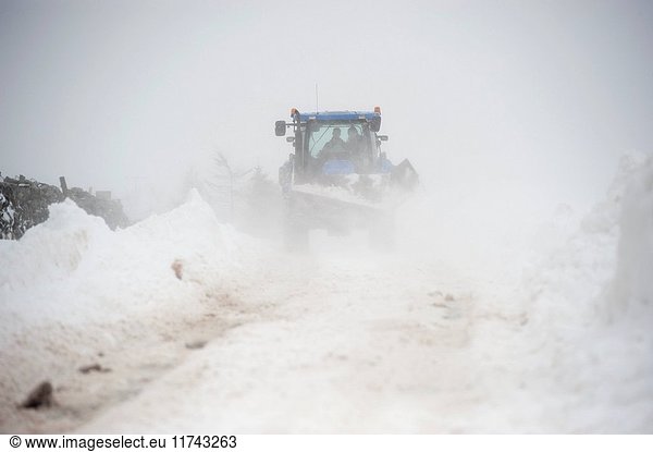 Farmer on a New Holland tractor clearing snow off rural road after a snowstorm. Cumbria  UK. (Photo by: Wayne Hutchinson/Farm Images/UIG)