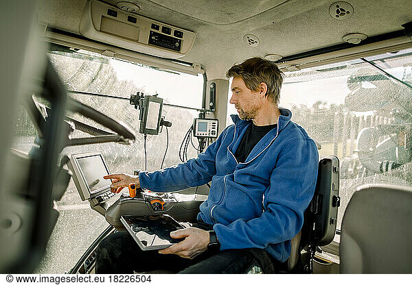 Farmer operating computer sitting in tractor at farm