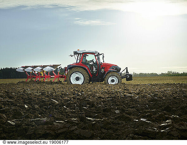 Farmer plowing field using tractor at sunrise
