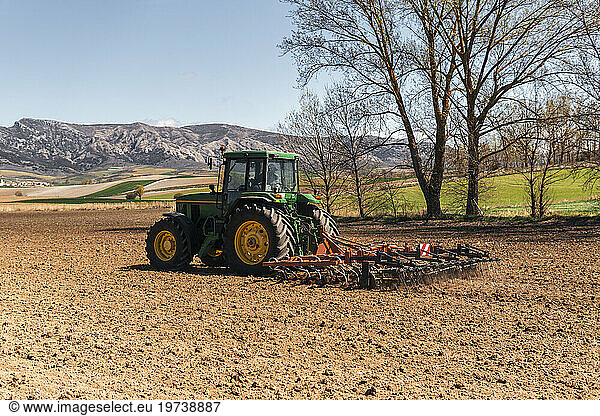 Farmer plowing field with tractor on sunny day