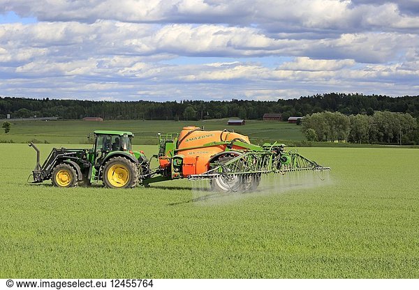 Farmer sprays wheat field with John Deere tractor and Amazone 5200 UX mounted sprayer on a beautiful day of summer. Salo  Finland - June 8  2018.