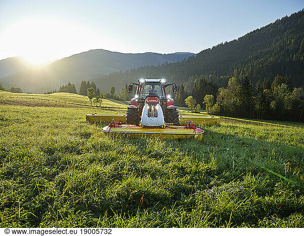 Farmer using tractor to mow field at sunrise