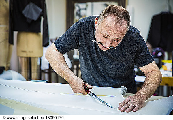 Fashion designer cutting fabric swatch at table in design studio