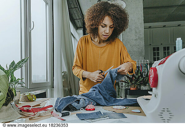 Fashion designer cutting jeans with scissors in workshop