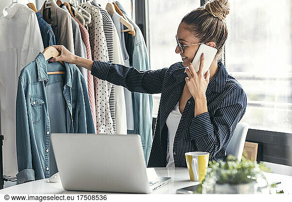 Fashion designer holding shirt and talking on mobile phone in office