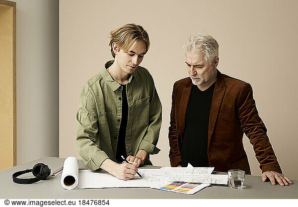 Fashion designer looking at trainee sketching in studio