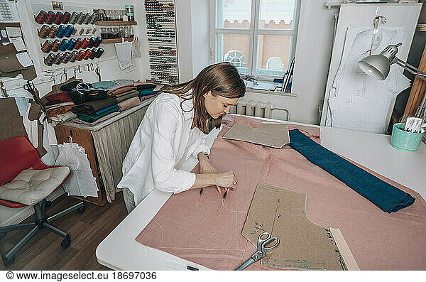 Fashion designer marking measurement on fabric at workshop