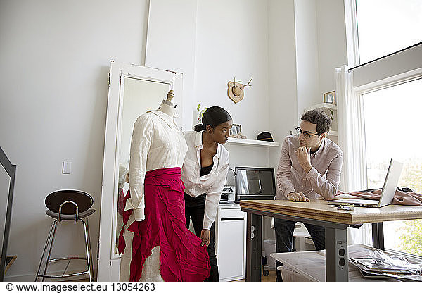 Fashion designer showing dress on model to colleague