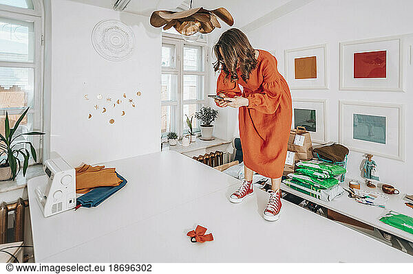 Fashion designer taking picture of product standing on workbench