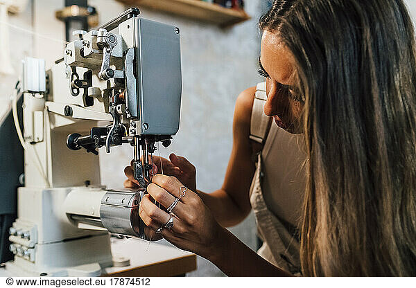 Fashion designer threading needle in sewing machine at workshop