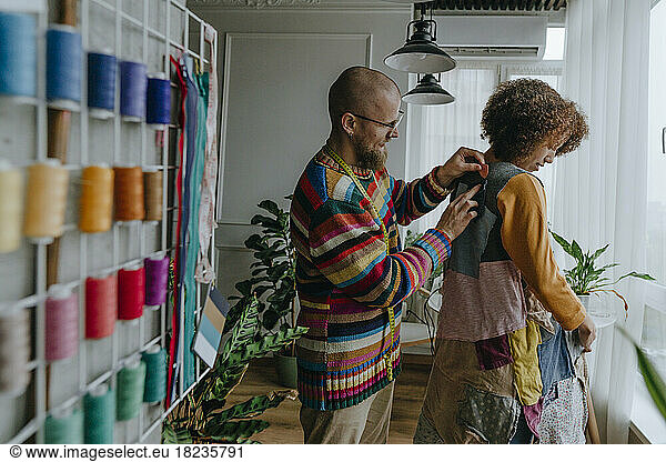 Fashion designer trying patchwork dress on colleague in workshop
