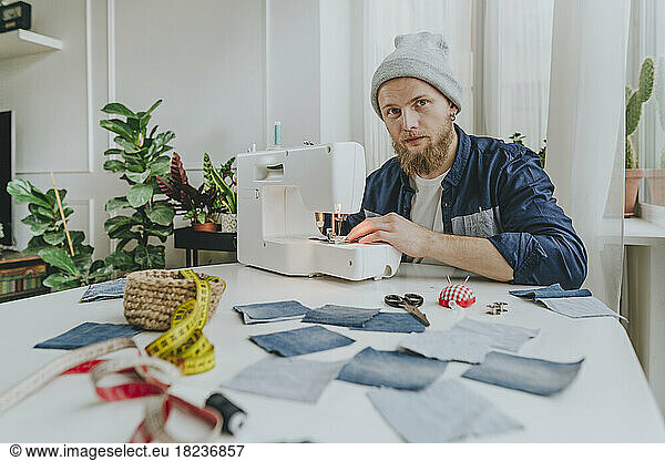 Fashion designer wearing knit hat sitting with sewing machine in workshop