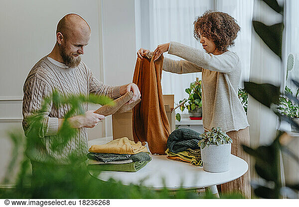 Fashion designer with colleague folding clothes on table