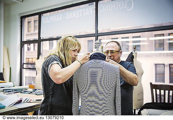 Fashion designers working on jacket against glass window in design studio