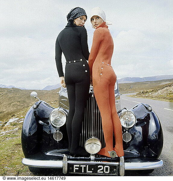 fashion  1960s  two young women in catsuit standing on veteran car  full length