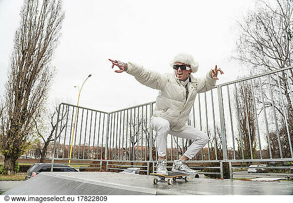Fashionable man gesturing on skateboard by railing