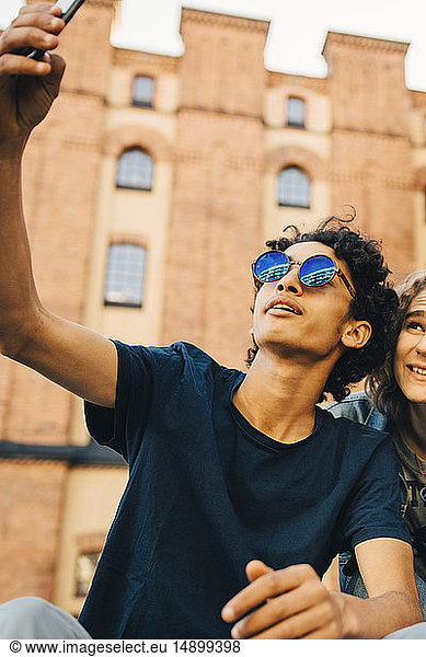 Fashionable teenage boy taking selfie with friend in city