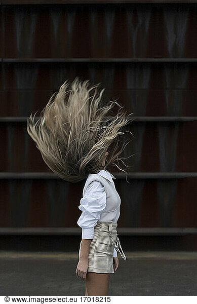 Fashionable woman with eyes closed tossing hair in front of wall