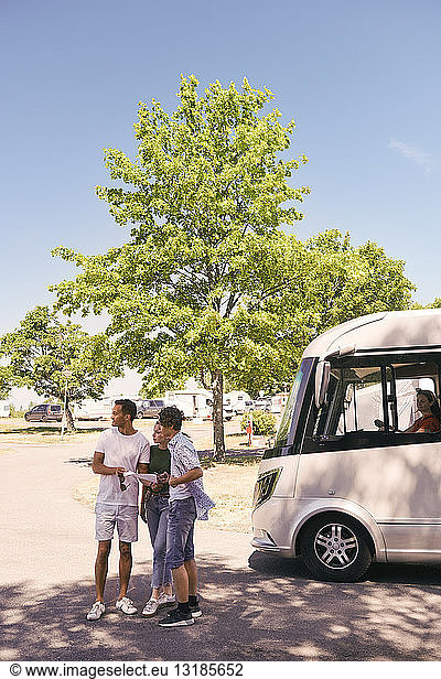 Father and children reading map while woman sitting in camper trailer at park