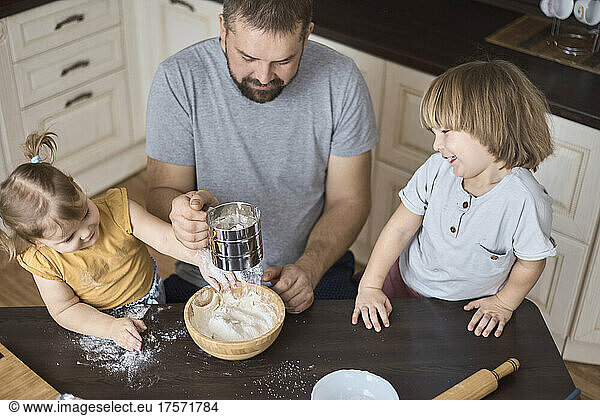 Father and children sifting flour for dough