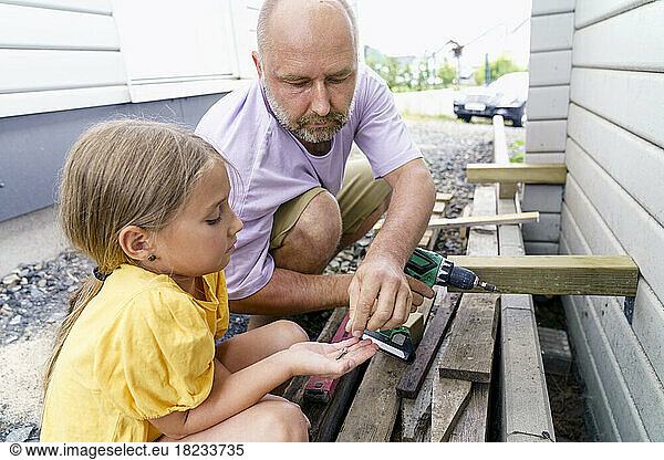 Father and daughter building wooden wall crouching outside house