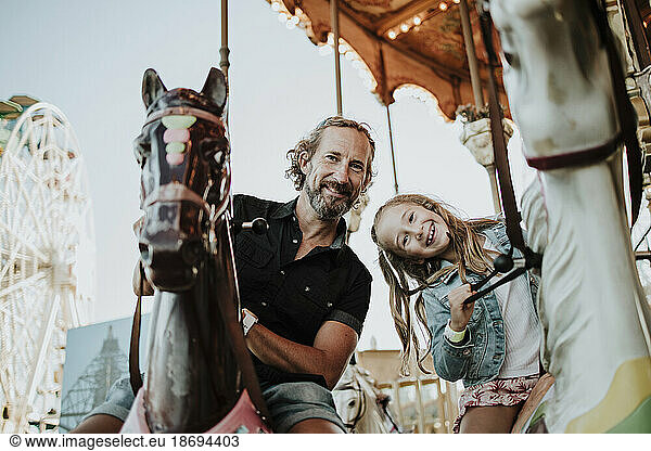 Father and daughter enjoying carousel ride at amusement park
