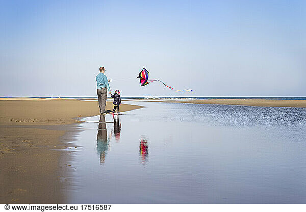 Father and daughter fly kite at beach in winter