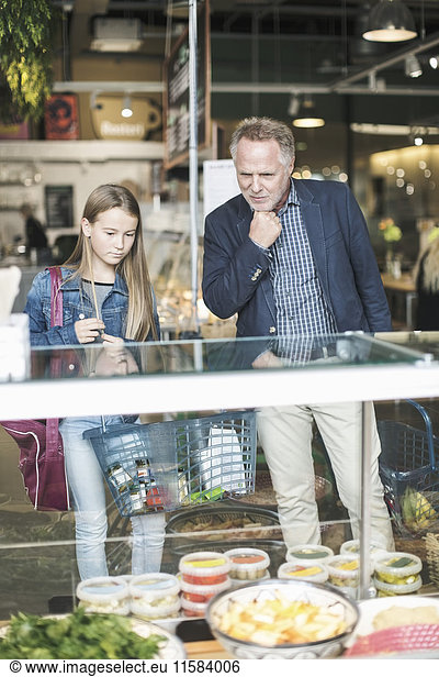 Father and daughter looking in display cabinet while shopping at supermarket