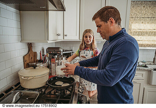 Father and daughter making pancakes in kitchen
